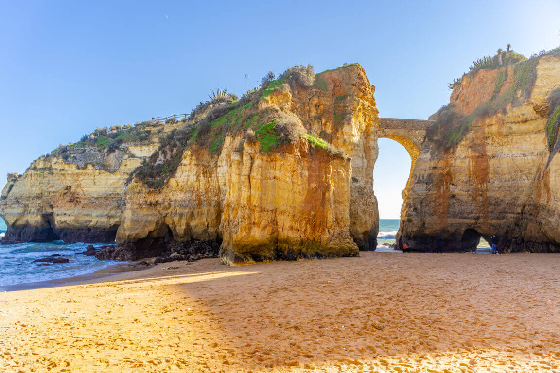 The historic Roman-style stone bridge framing the sandy beach cove of Praia dos Estudantes in Lagos