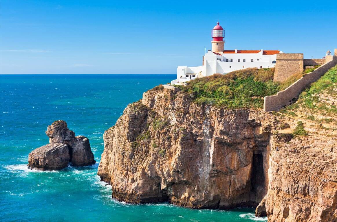 The iconic isolated lighthouse structure standing atop towering vertical cliffs at Cape St. Vincent near Sagres